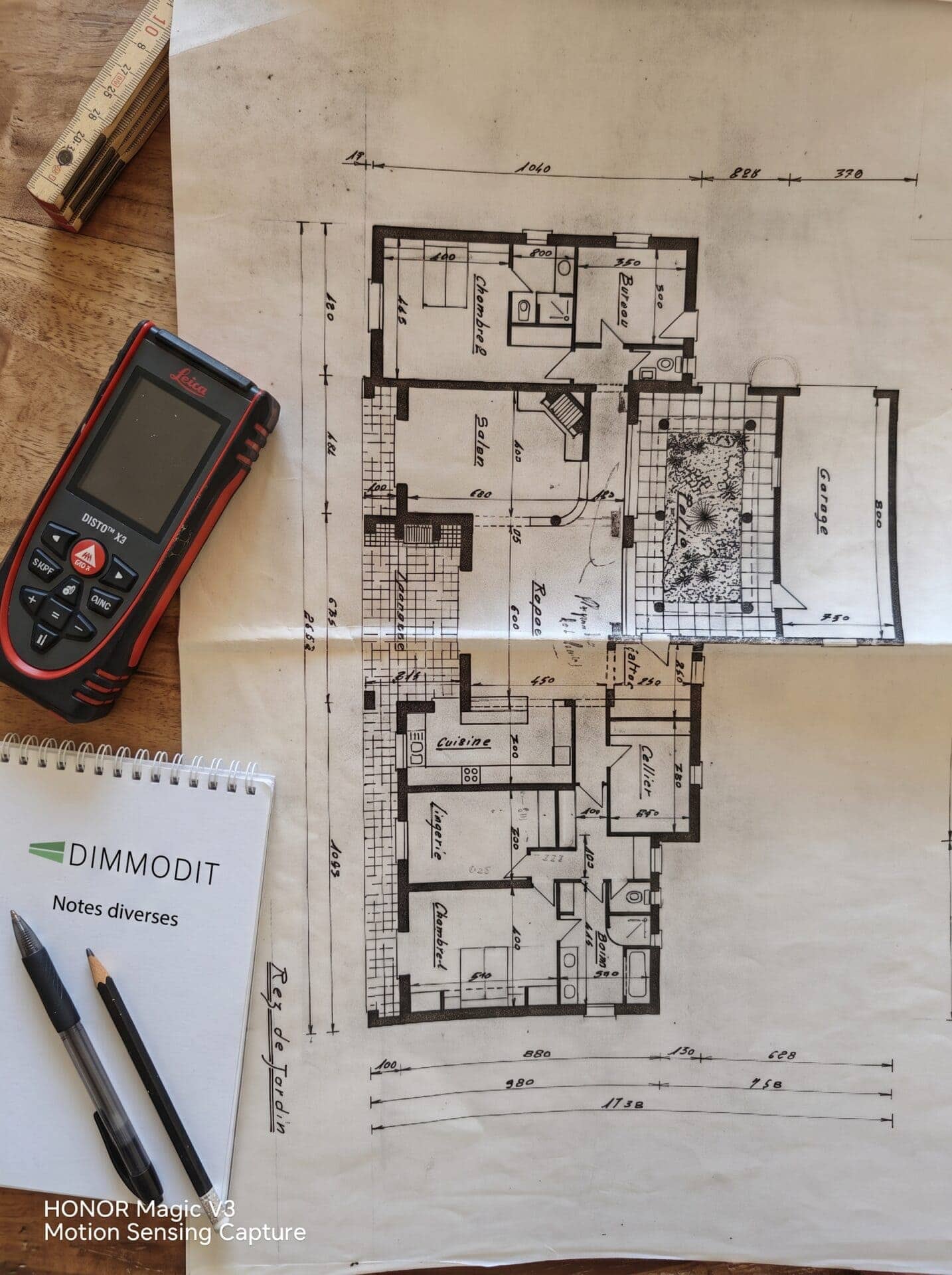 Plan d'architecte annoté, télémètre laser Leica et carnet de notes Dimmodit utilisés pour le calcul précis des surfaces Carrez, habitable (Boutin) et de référence DPE lors d'un diagnostic immobilier.